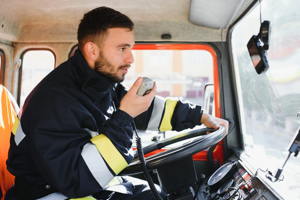 Firefighter using portable radio set in fire truck, space for text